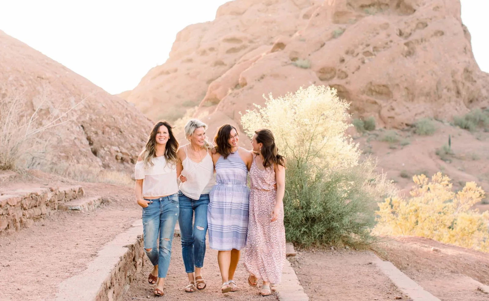 Four women walking together through a sunlit desert landscape